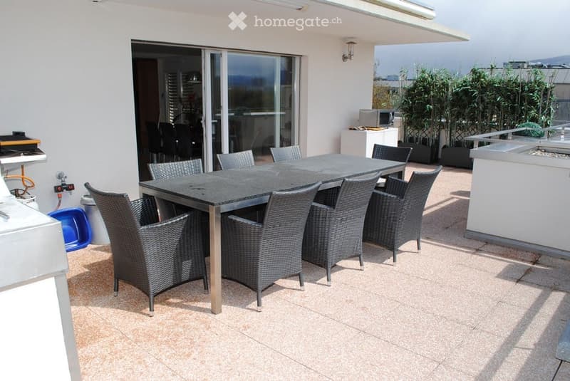 Terrace with a black dining table and wicker chairs, sliding glass doors leading inside, small plants, and a modern outdoor setup.