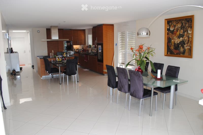 Open-plan kitchen and dining area with white tiled flooring, wooden cabinets, stainless steel appliances, and a glass dining table with six dark upholstered chairs.