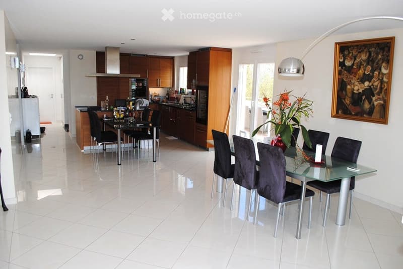 Open-plan kitchen and dining area with white tiled flooring, modern wooden cabinets, stainless steel appliances, and a glass dining table with black chairs.