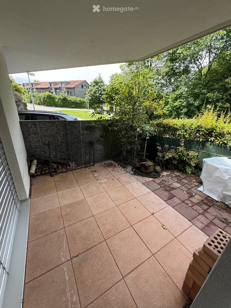 Balcony with tiled floor, metal gate, and some greenery in the background.