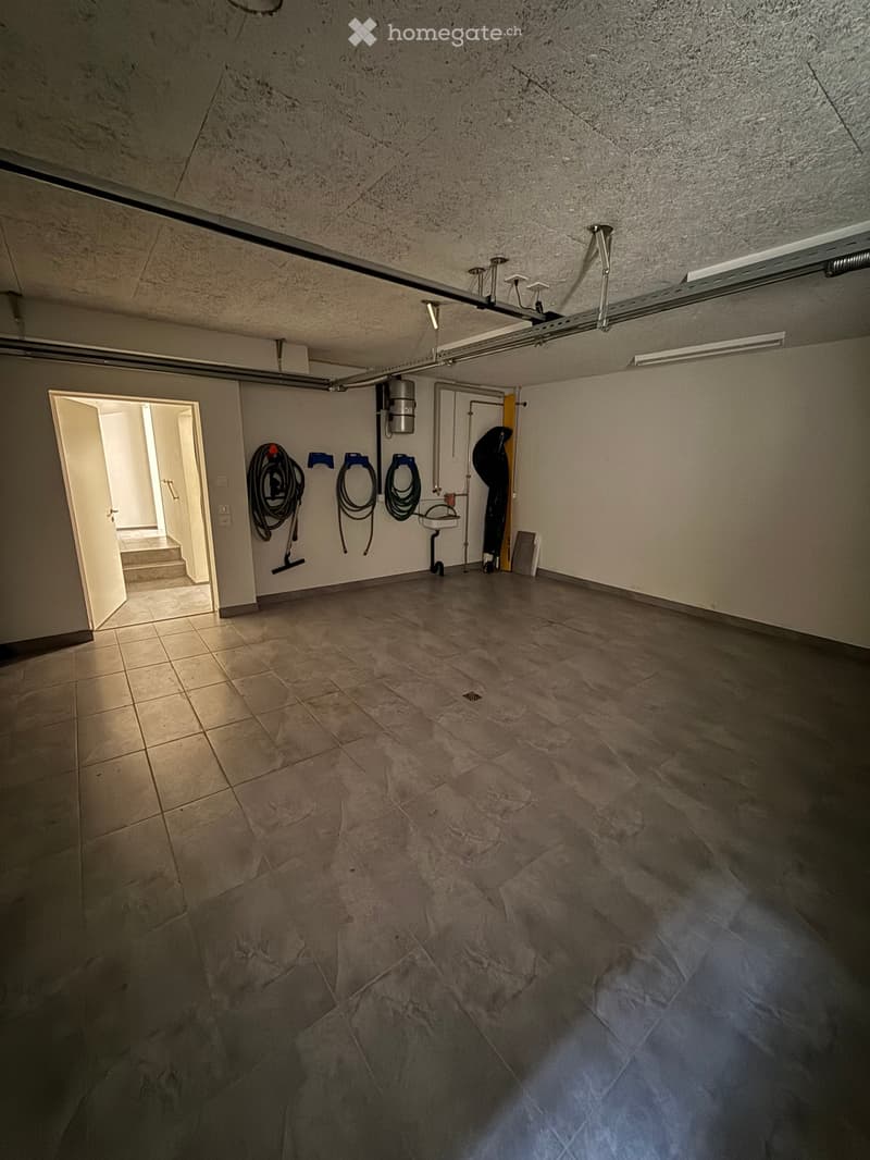 Empty room with tiled floor and concrete walls, featuring a doorway leading to another area and some storage items in the background.