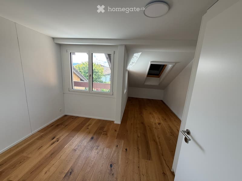 Empty hallway with wooden flooring, white walls, and a skylight window at the end.