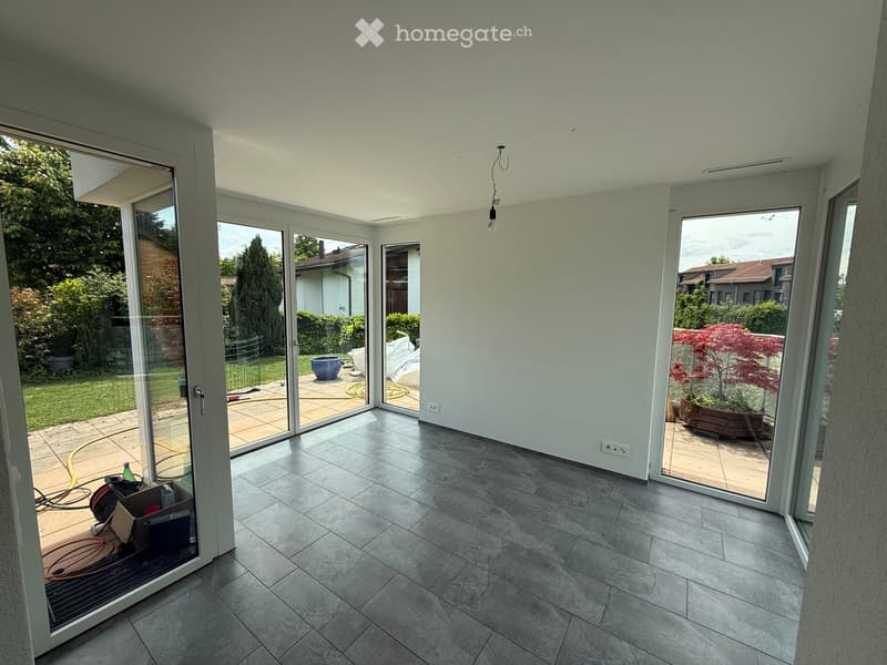 Empty room with large sliding glass doors leading to a patio, tiled floor, and visible outdoor area with plants and a hose.
