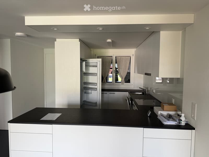 Modern kitchen with white cabinets, black countertop, stainless steel sink, and refrigerator. There are some papers and a small box on the counter.
