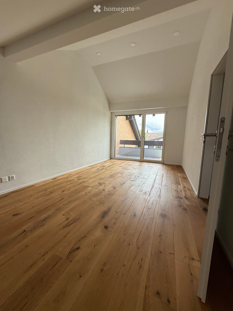 Empty room with wooden flooring, white walls, and a sliding glass door leading to a balcony.