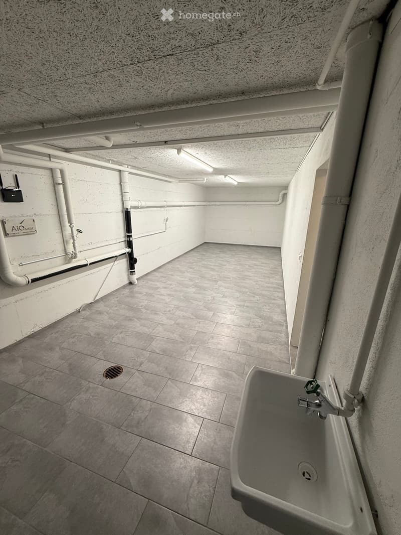 Utility bathroom with tiled floor, concrete walls, exposed pipes, and a single sink with a faucet.