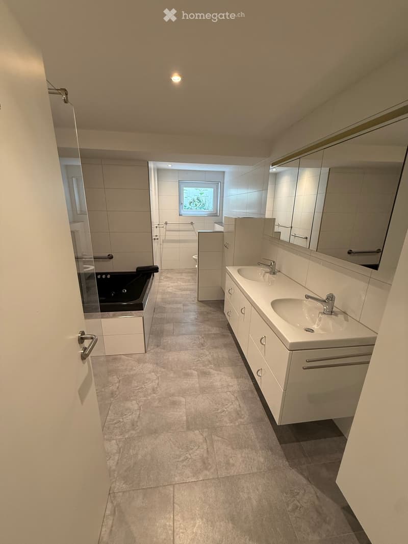 Modern bathroom with a double sink vanity, large mirror, bathtub, and a window providing natural light.