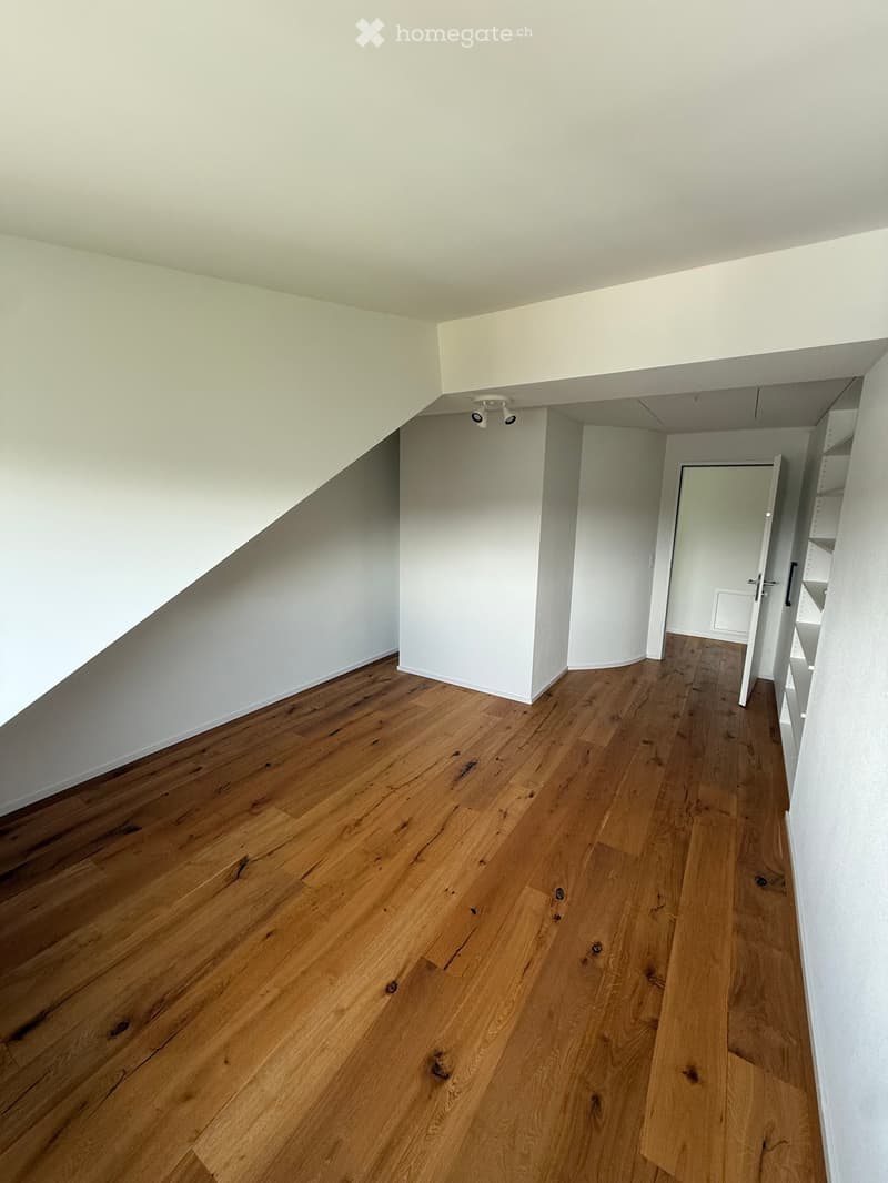 Empty hallway with wooden flooring and white walls, featuring a door at the end and a built-in shelf unit on the right side.