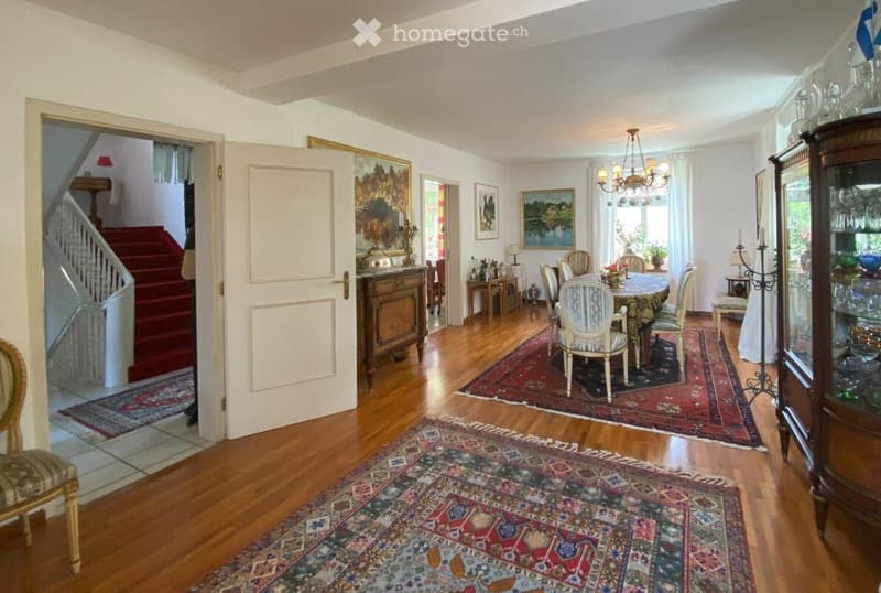 Elegant dining room with wooden floors, ornate dining table and chairs, chandelier, side tables, and decorative items.
