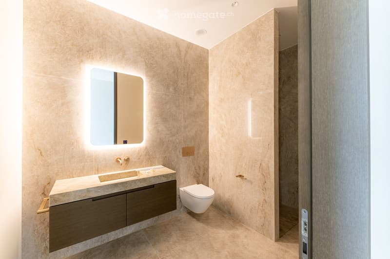 Modern bathroom with beige marble walls and floor, a floating vanity with dark wood cabinets, a sleek sink, a toilet, and a backlit mirror above the sink.