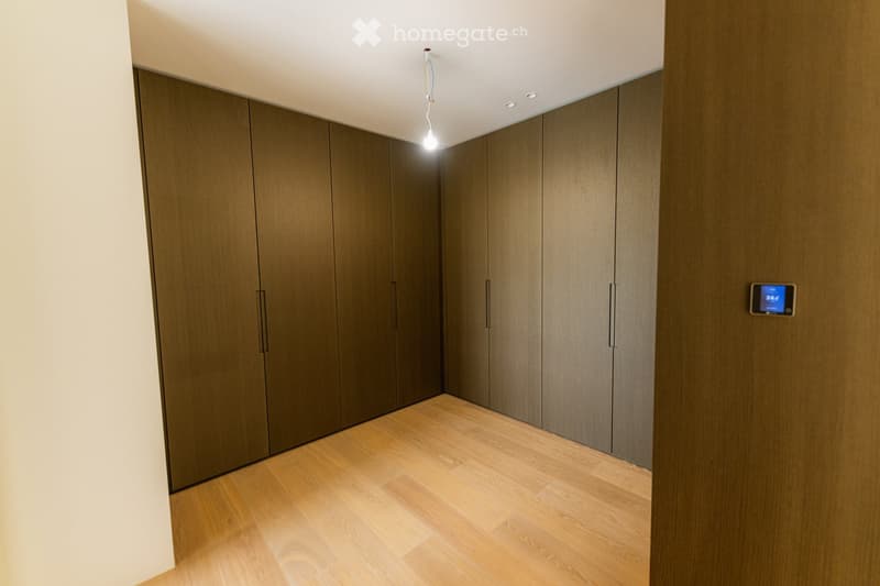 Empty hallway with wooden floor and dark wooden panel walls, featuring recessed ceiling lights and a digital display on the wall.