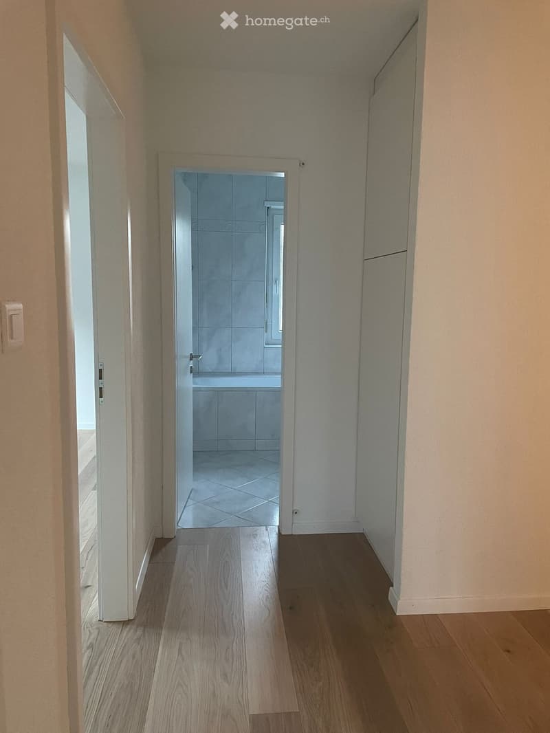 Empty hallway with wooden floor, white walls, open door to bathroom with bathtub