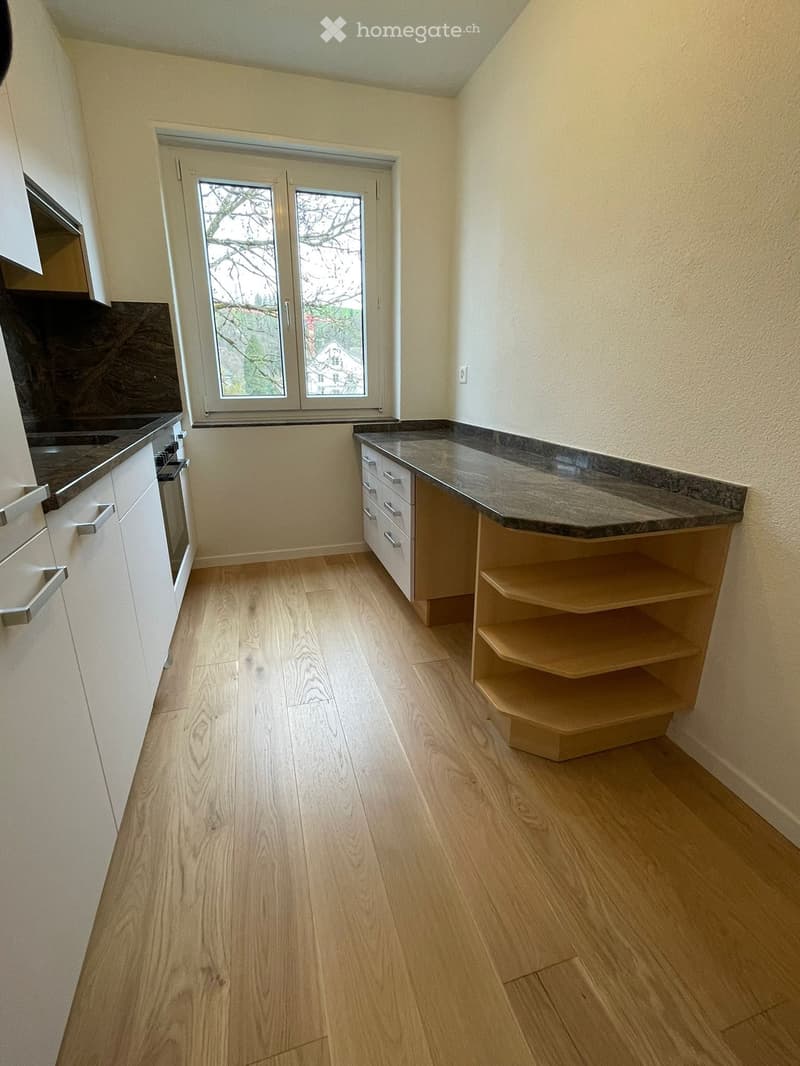 Modern kitchen with light wooden flooring, white cabinets, granite countertop, and built-in oven and sink.