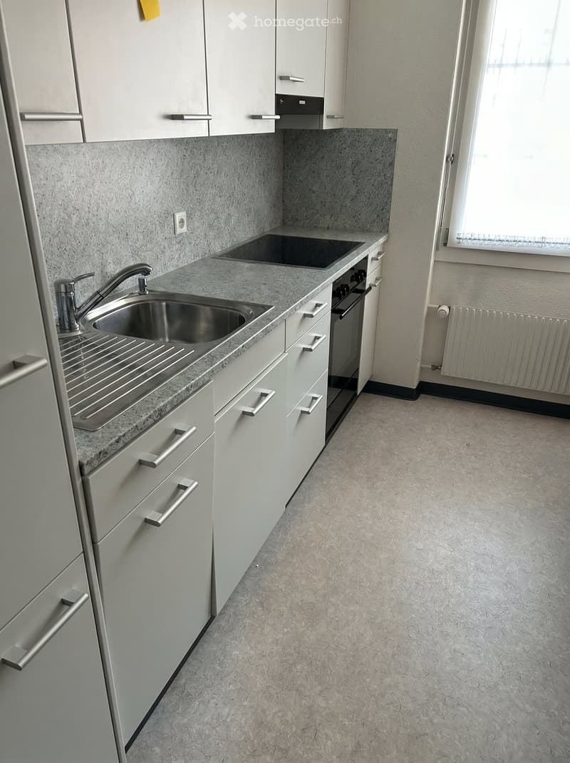 Modern kitchen with white cabinets, granite countertop, double sink, and built-in oven. Light grey flooring and large window provide natural light.