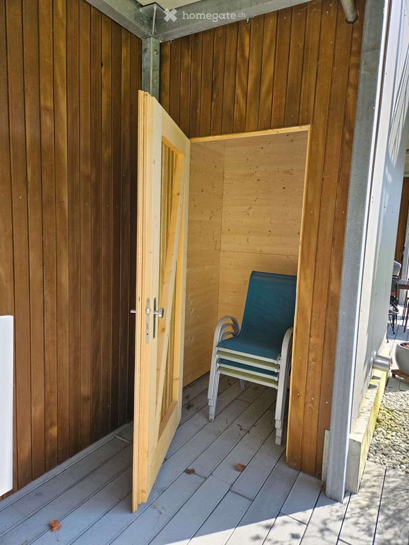 Balcony with wooden walls, grey decking, and a single green folding chair.