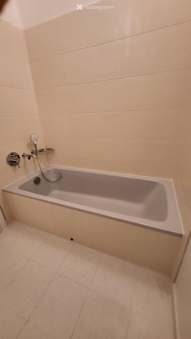 Modern bathroom with a white bathtub, tiled walls, and a showerhead attached to the wall.