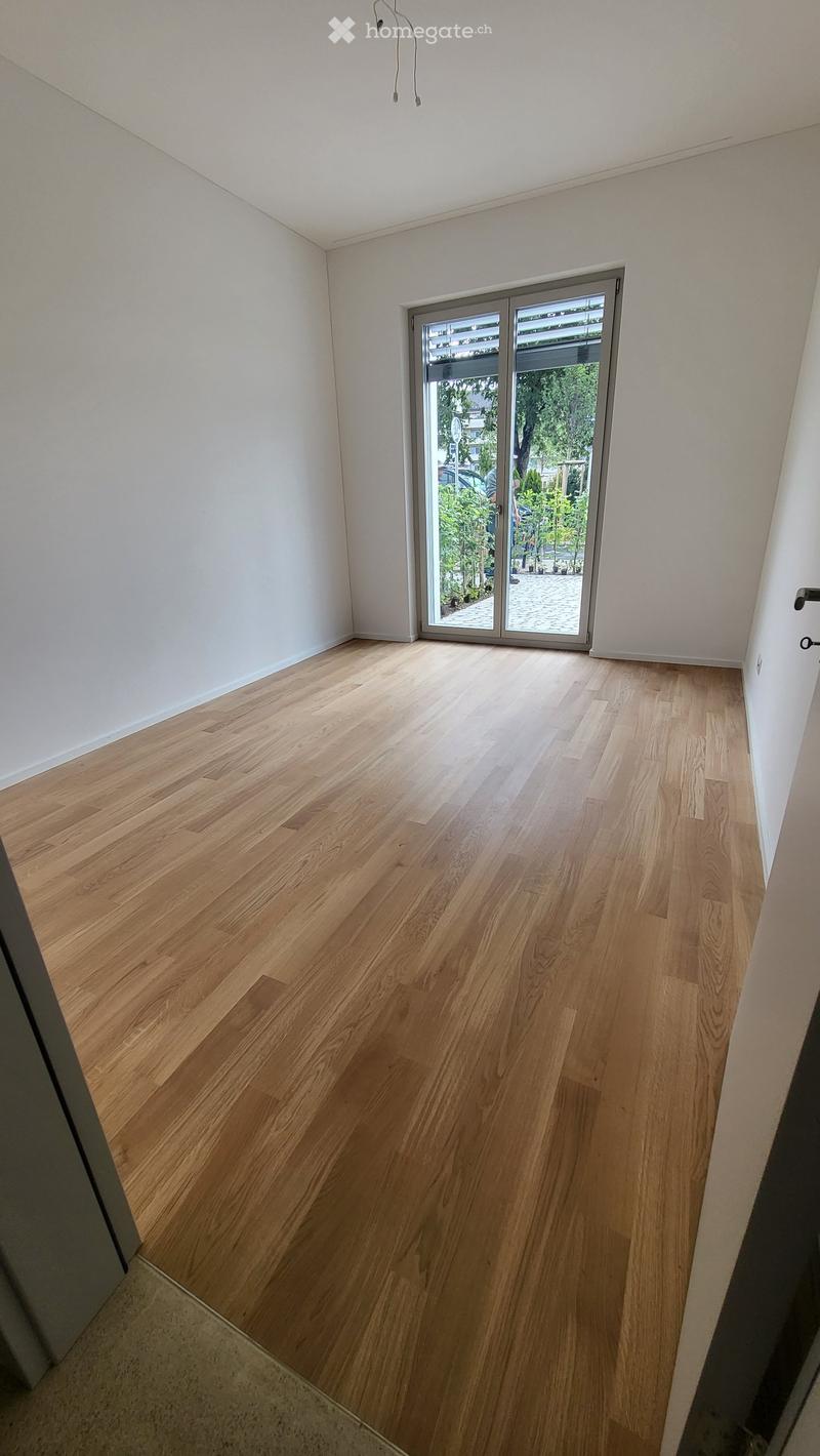 Empty room with light wooden flooring and white walls, featuring a large sliding glass door leading to an outdoor area.