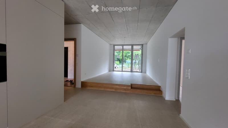 Empty room with white walls, concrete floor, and large glass doors leading to an outdoor area. No furniture or equipment present.