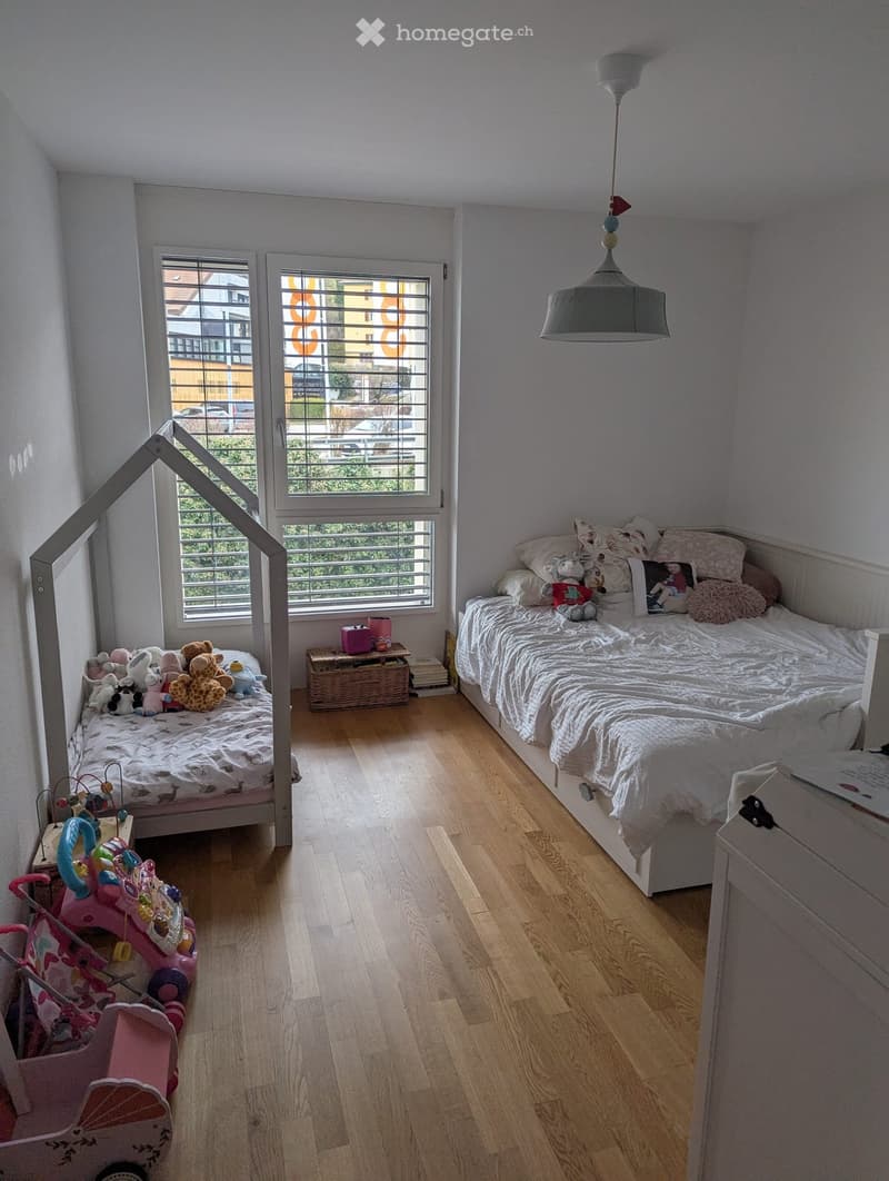 Cozy children's bedroom with two single beds, stuffed toys, a wicker basket, and a hanging lamp.