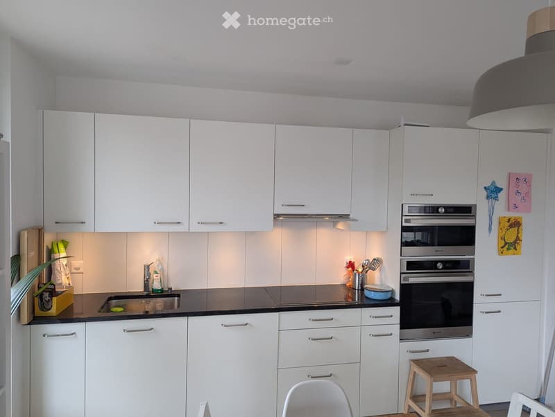 Modern kitchen with white cabinets, stainless steel appliances, and a black countertop. Includes a sink, oven, and small wooden stool.