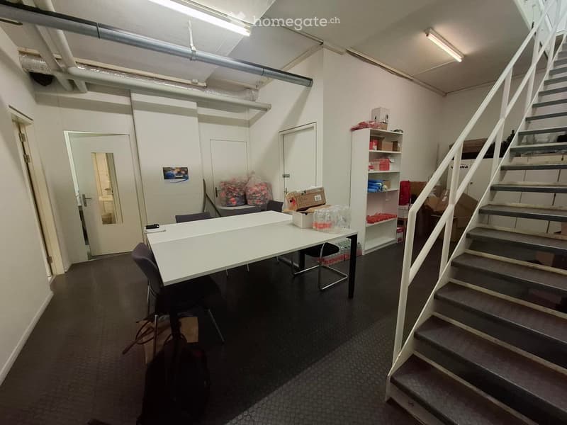 Office space with a white desk, chairs, shelves, and a staircase leading upwards.