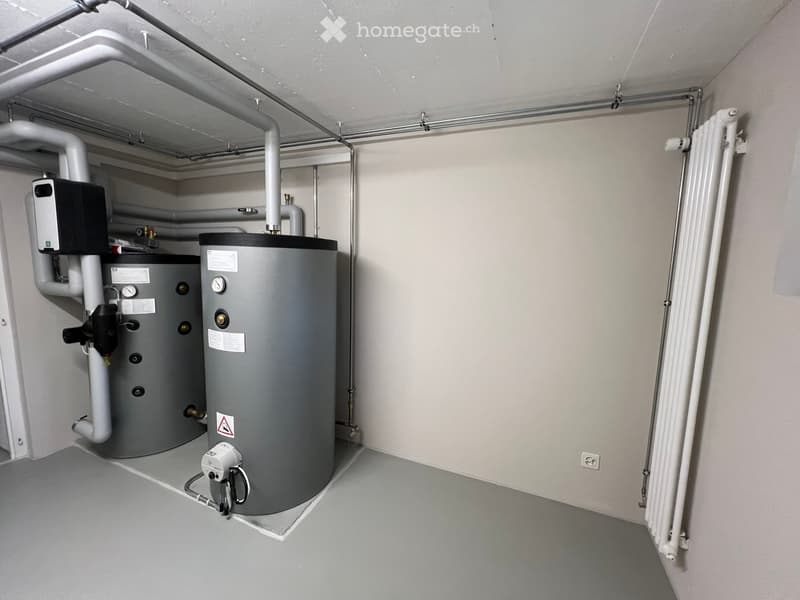 Utility room with a water heater, radiator, and various pipes and valves.