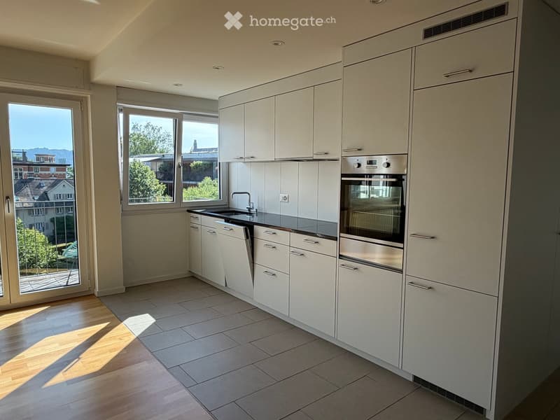 Modern kitchen with white cabinets, stainless steel appliances, and large windows offering a view of the city.