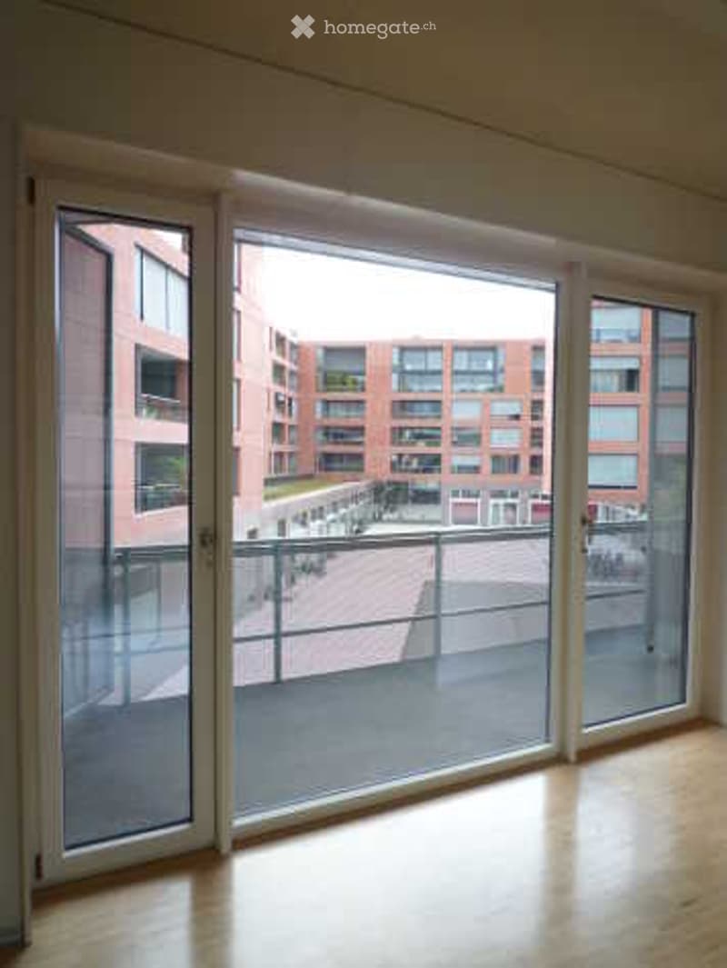 Empty room with large sliding glass doors leading to a balcony, wooden floor, and modern white walls.