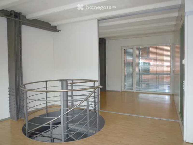 Empty room with a modern spiral staircase, wooden flooring, and large glass doors leading to an outdoor area.