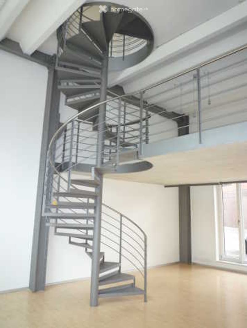 Modern interior with a sleek, black spiral staircase featuring a metal railing, leading to an upper level with a glass balcony overlooking the space.