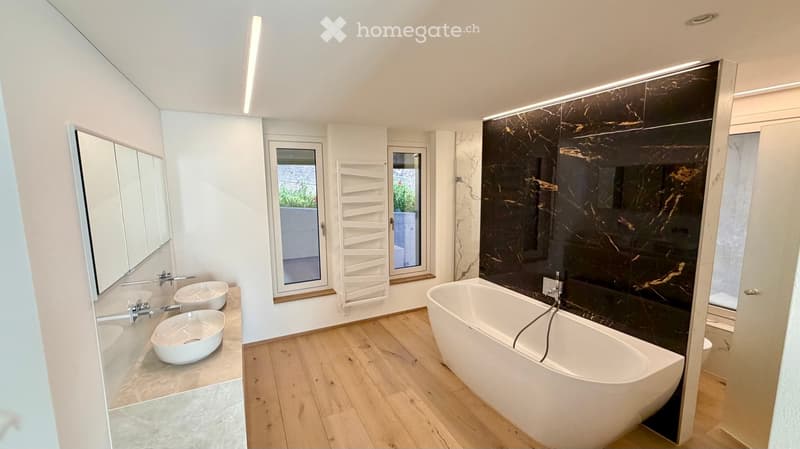 Modern bathroom with a freestanding bathtub, two sinks, a large mirror, and a window with a view of greenery.