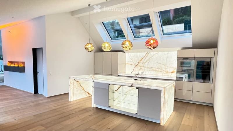 Modern kitchen with a large island, marble countertops, built-in cabinets, and pendant lights. Features a sleek fireplace on the left side and a double oven on the right.