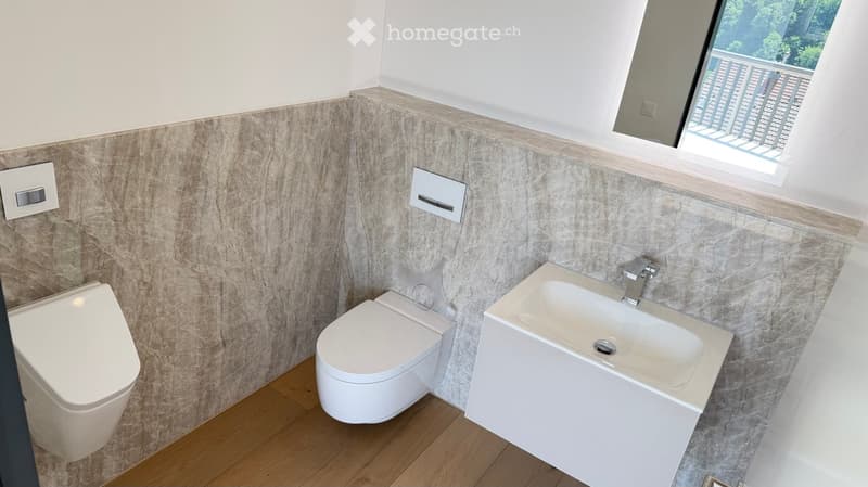 Modern bathroom with white toilet, sink, and faucet, marble wall tiles, and a small window with a view of a balcony.