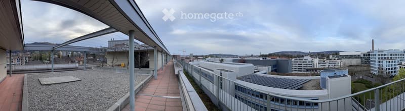 Rooftop terrace with a paved walkway, gravel area, and modern buildings in the background.