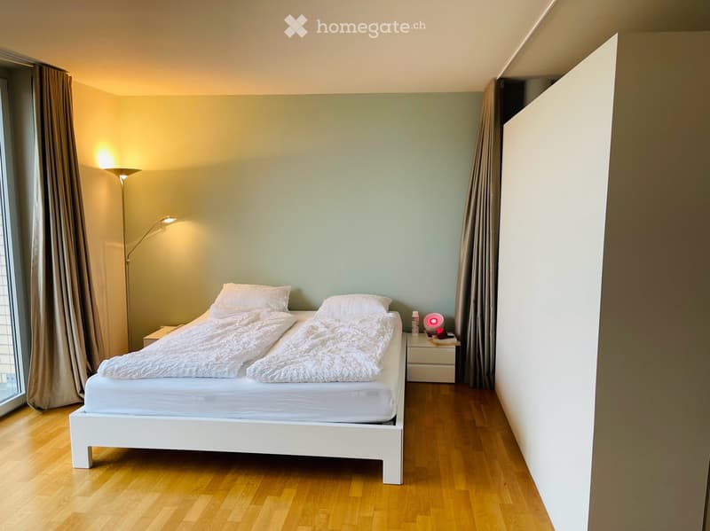 Modern bedroom with a white bed, nightstand, and floor lamp. Light green walls and wooden flooring.