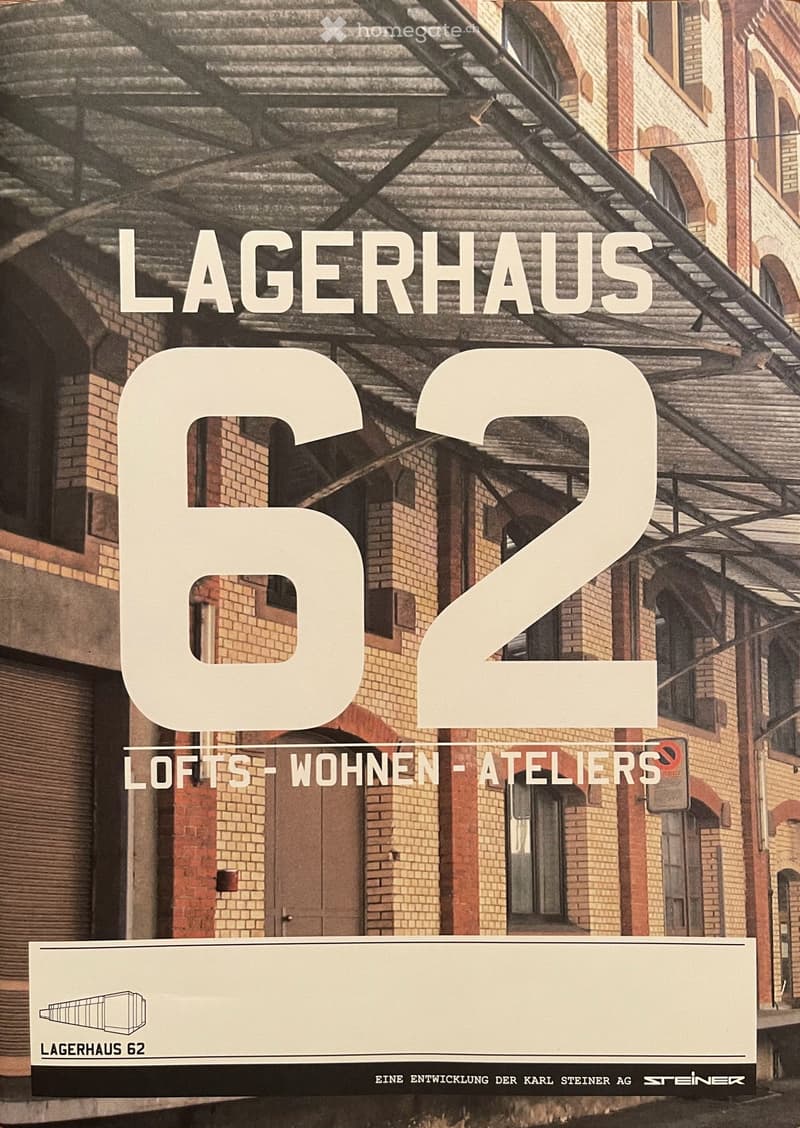 Facade of a brick building with arched windows and a metal roof structure, featuring large text overlay reading "LAGERHAUS 62" and "LOFTS-WOHNEN-ATELIERS".