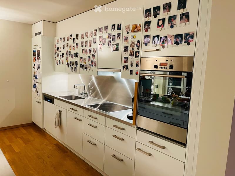 Modern kitchen with white cabinets, stainless steel appliances, and a wooden floor. Photos are pinned to the refrigerator.