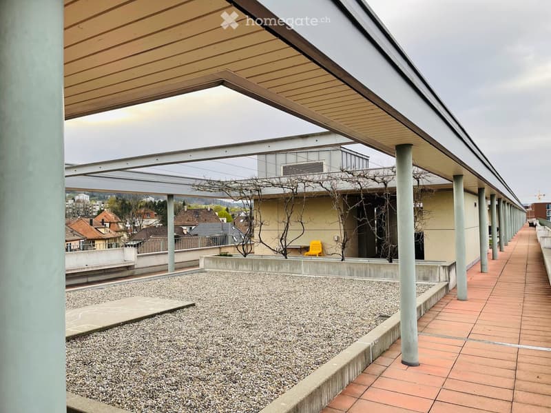 Covered outdoor balcony with gravel area, tiled walkway, and distant cityscape view.
