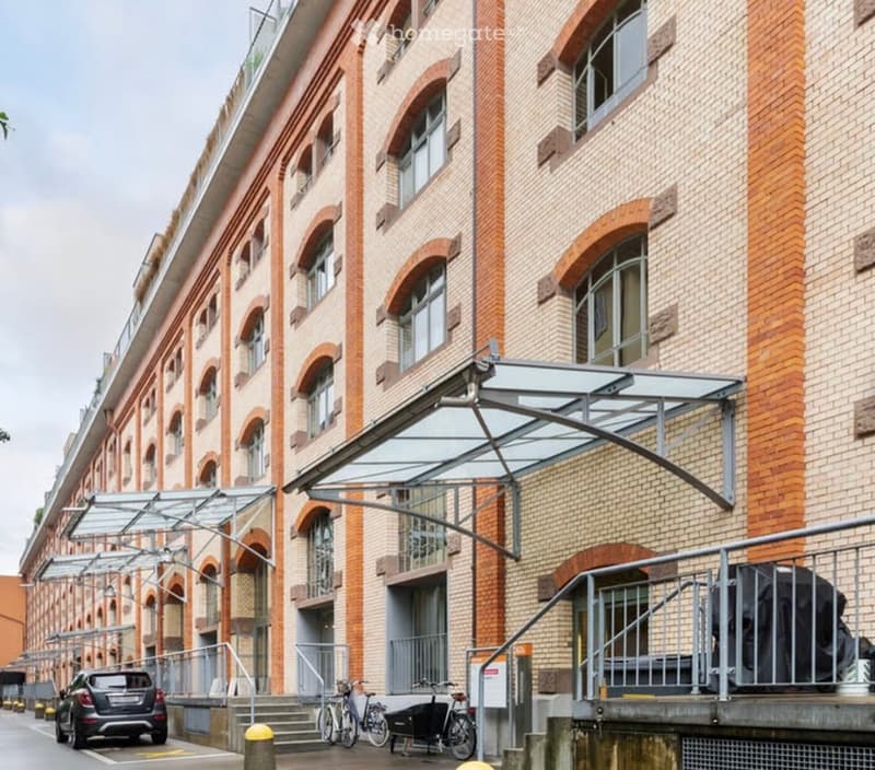 Modern multi-story building with brick facade, large arched windows, and covered entrance area with glass canopy.