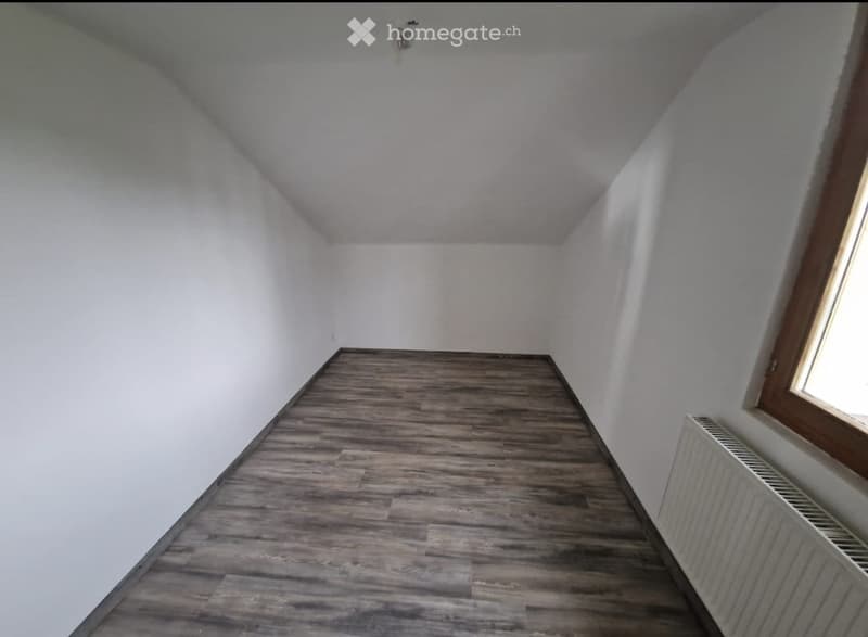 Empty room with wooden flooring, white walls, and a single window with wooden frame. No furniture or equipment present.