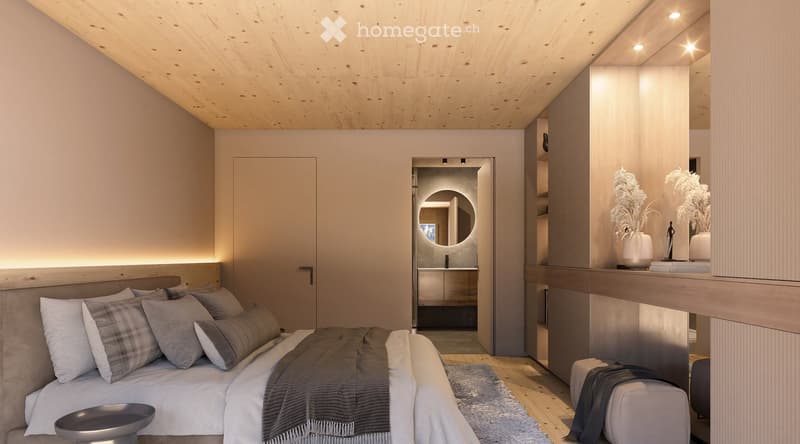 Modern bedroom with a wooden ceiling, a large bed with pillows and blankets, a small stool, a vase with dried plants, a sculpture, and an open bathroom area with a round mirror and sink.