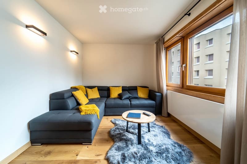 Modern living room with a grey sectional sofa, yellow throw pillows, a small round coffee table, a fur rug, and large windows with wooden frames.