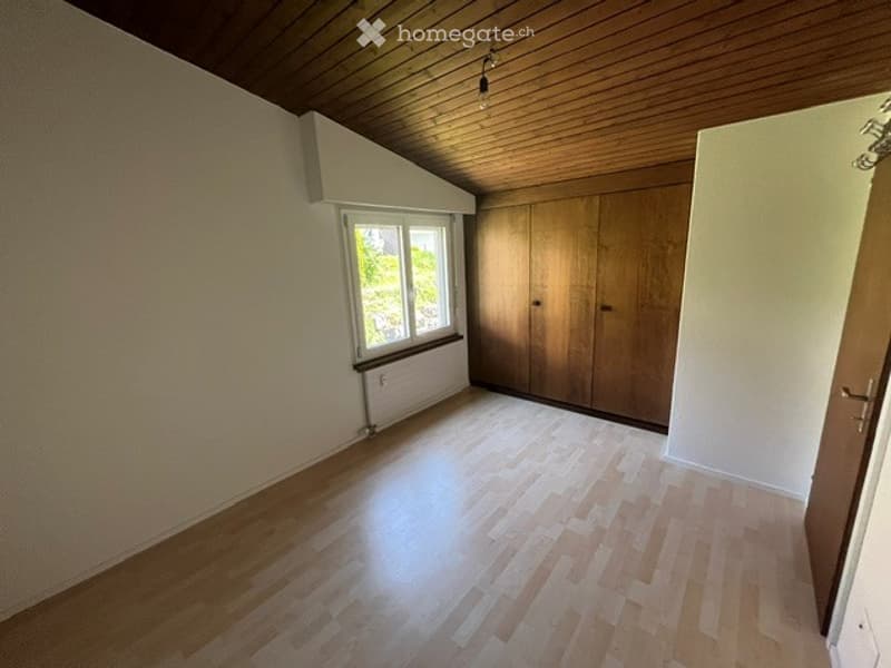 Empty room with wooden flooring, white walls, large window, and built-in wooden closet.
