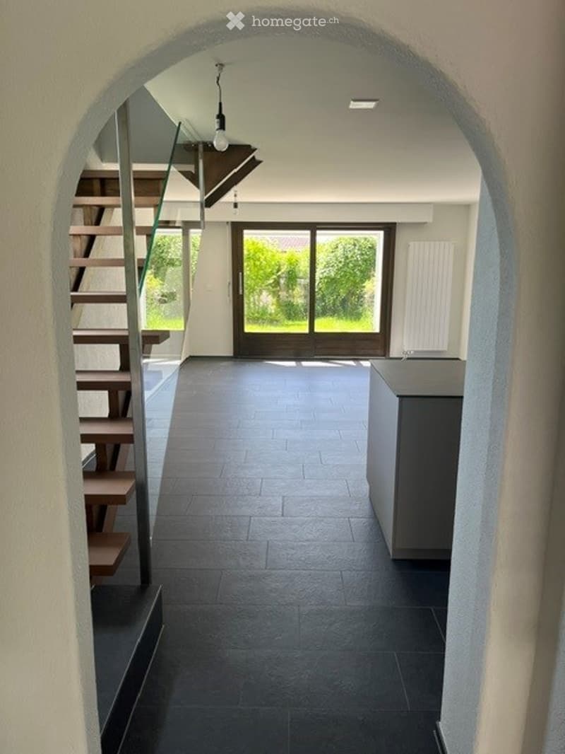 Modern hallway with dark tiled floor, glass sliding doors leading to outdoor area, staircase with wooden steps and metal railing, minimalist design.