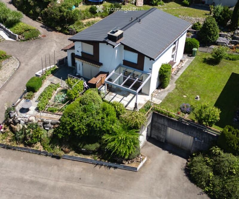 Two-story house with a modern design, featuring a garage, a well-maintained garden, and a covered patio area.