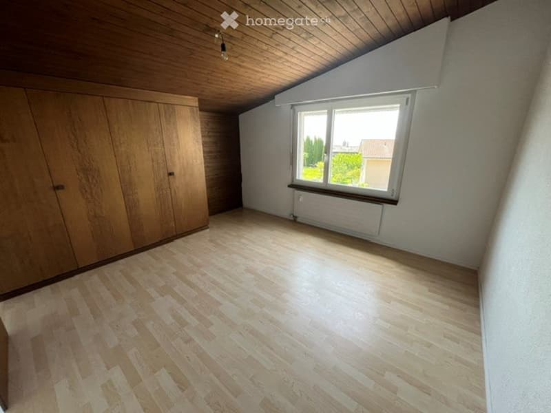 Empty room with wooden flooring, white walls, large window, and built-in wooden closet.
