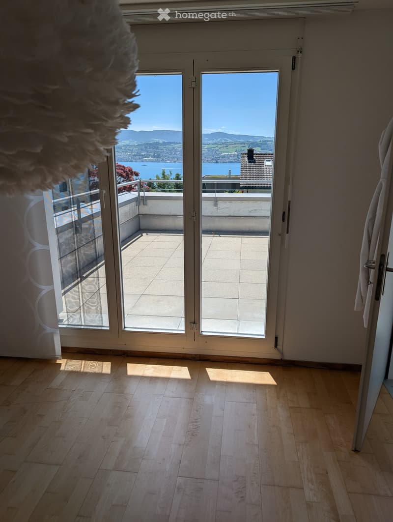 Empty room with wooden flooring, large glass doors leading to a balcony with scenic mountain and lake views.