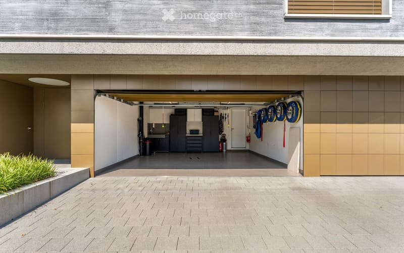 large garage with shelves, tires, storage boxes, workbench, trash can, fire extinguisher
