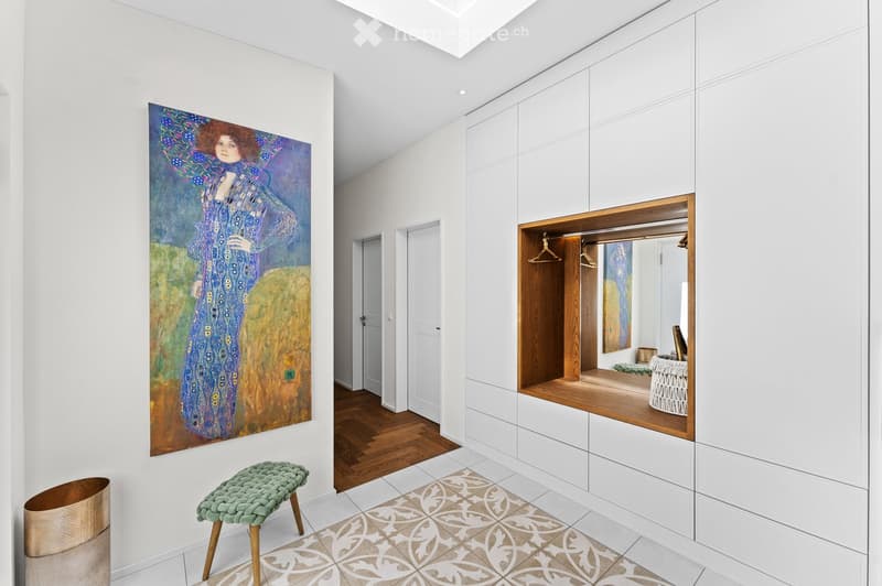 Modern white minimalist room with artwork, a rug, wooden floor, white cabinetry, a wooden bench, a wooden wastebasket.