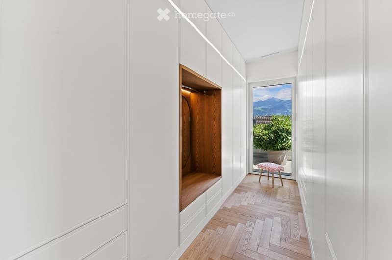 white walls, wooden flooring, built-in wardrobe, glass door leading to a balcony, a small stool, and a potted plant